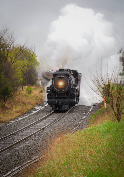 Steam train rounds curve on a rainy day.