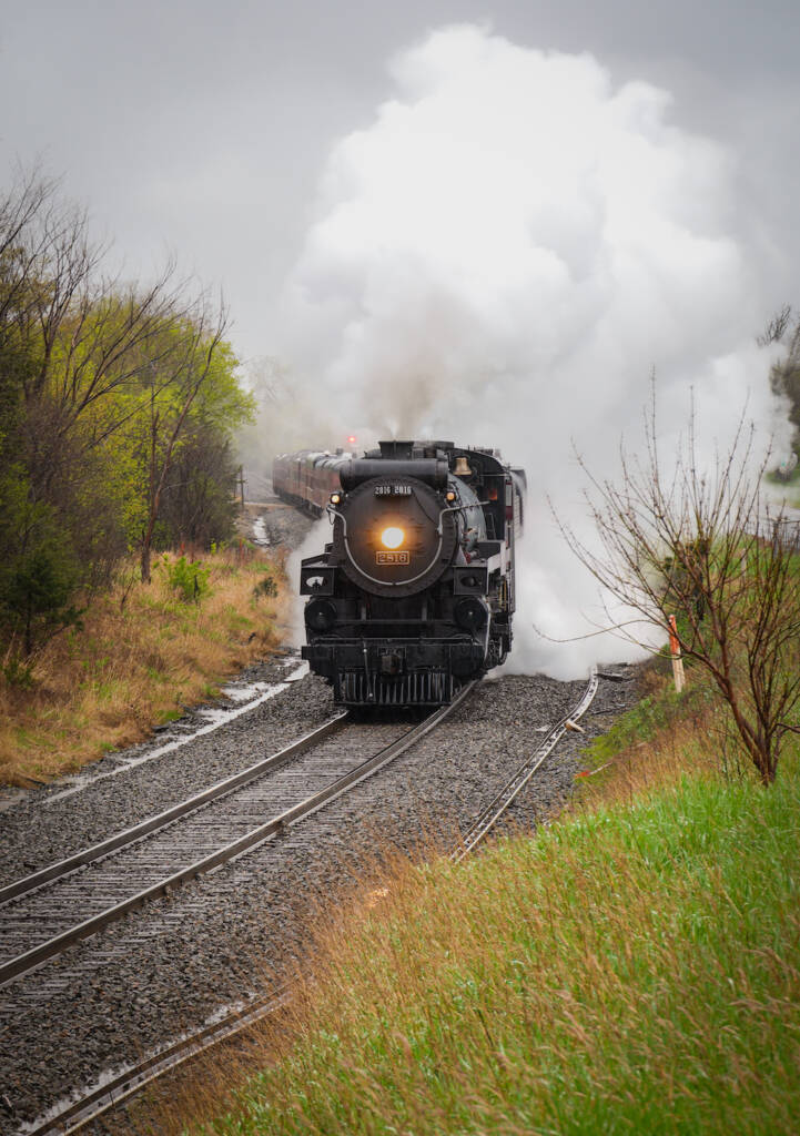 Steam train rounds curve on a rainy day.