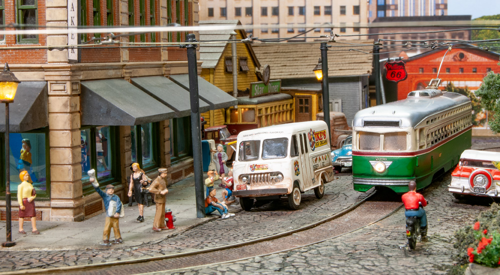 City pedestrians congregate around an ice cream truck while a green trolley swings around the corner