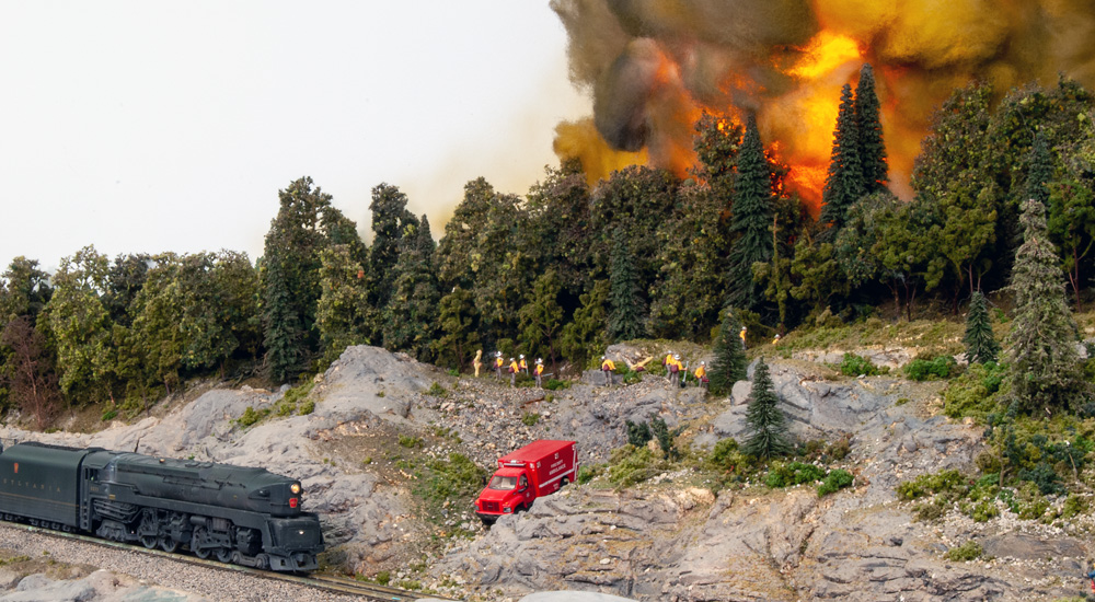 Firefighters work to contain a forest fire on a hillside above a railroad track