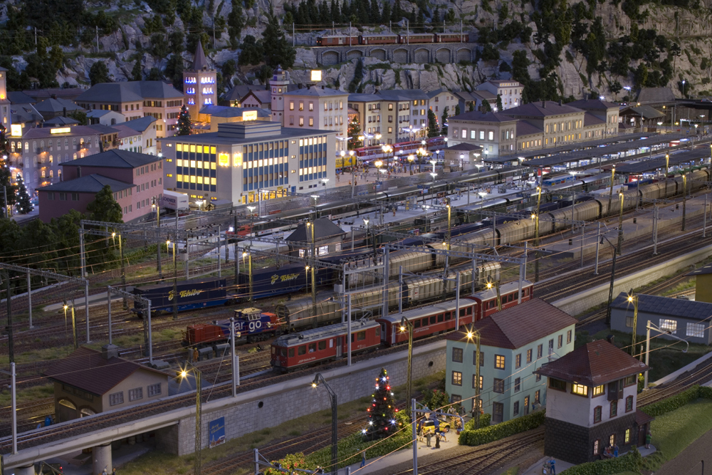 Large scale European-themed railyard at night with lights everywhere