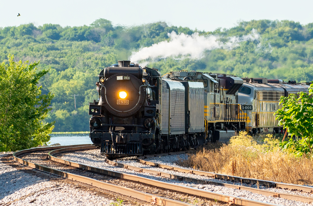 Steam engine and train round curve with river in background