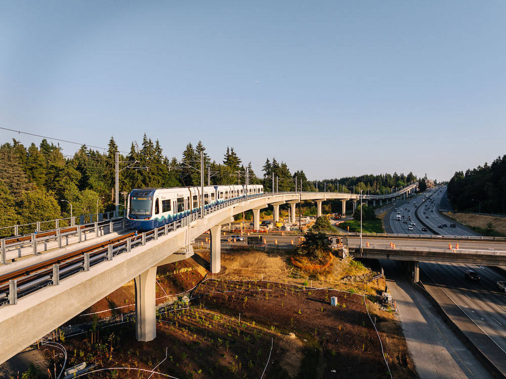 Light rail train on elevated right of way next to highway