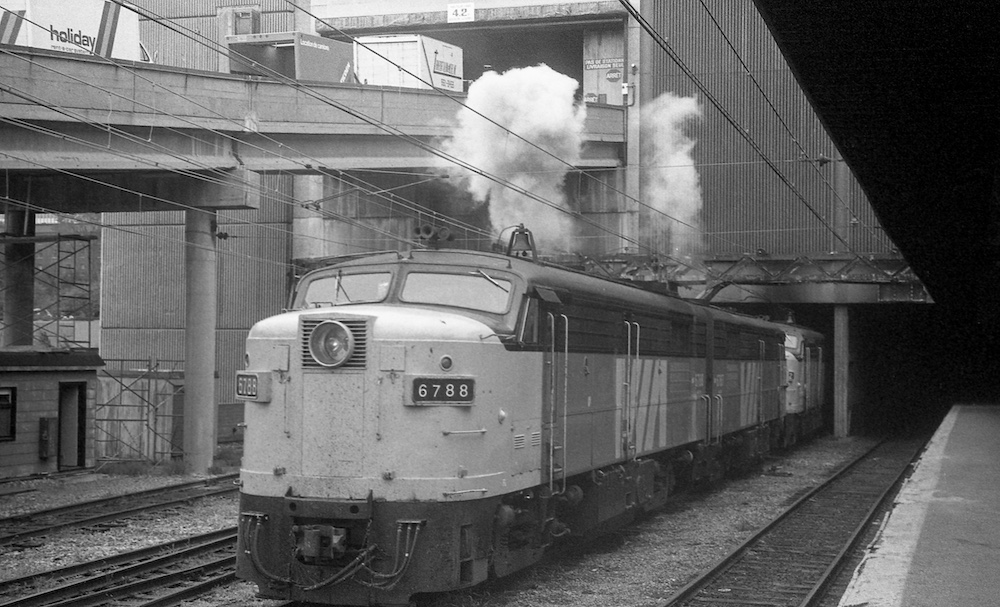 Black and white image of a passenger locomotive in urban surroundings