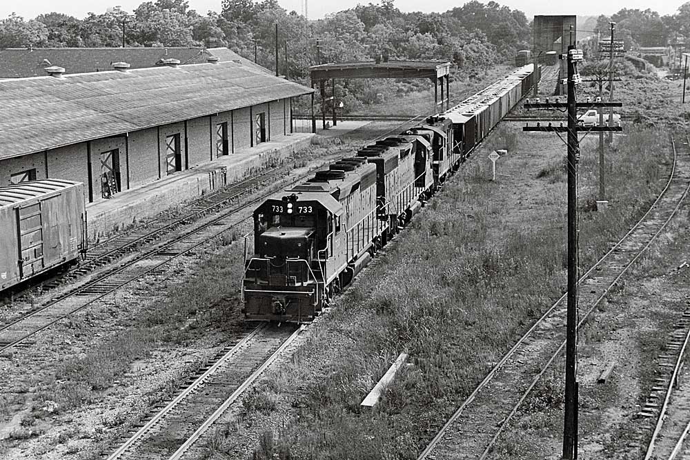 Three black diesel Atlanta & West Point locomotives with freight train by building with loading dock