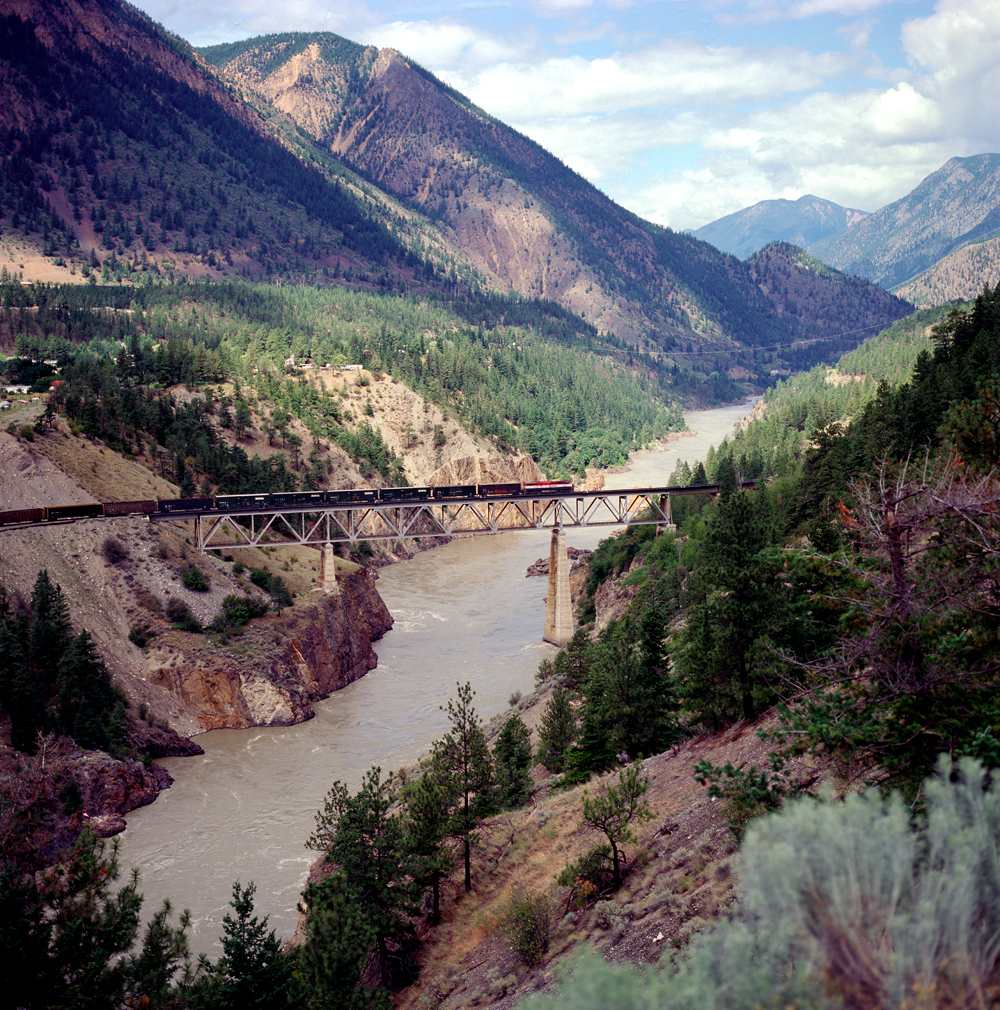 train on bridge above water with mountains