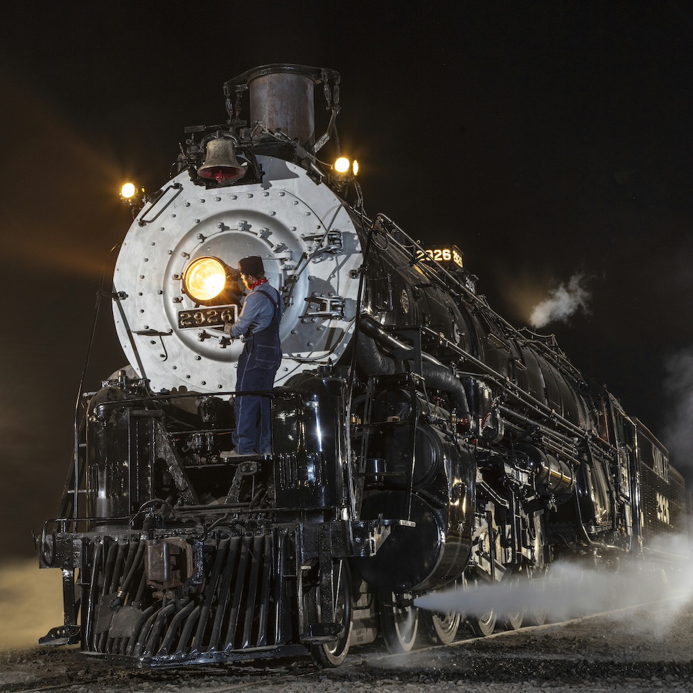 Steam locomotive at night with crew member up on the front