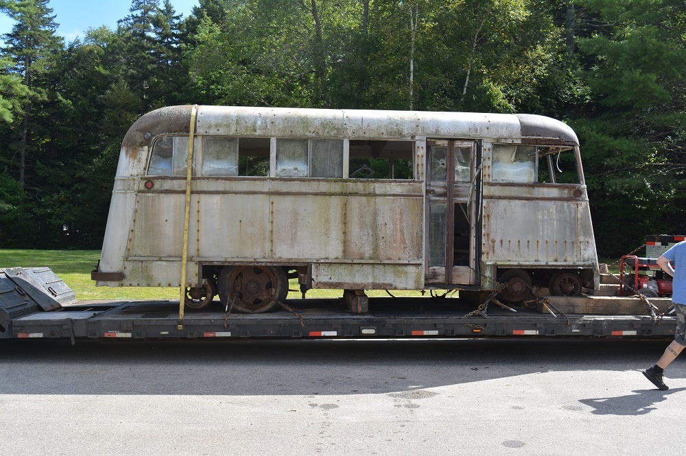 Old looking trolley/bus vehicle sitting on a trailer