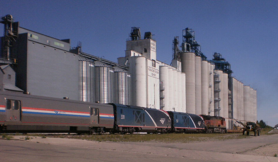 Going-away view of passenger train passing grain elevators
