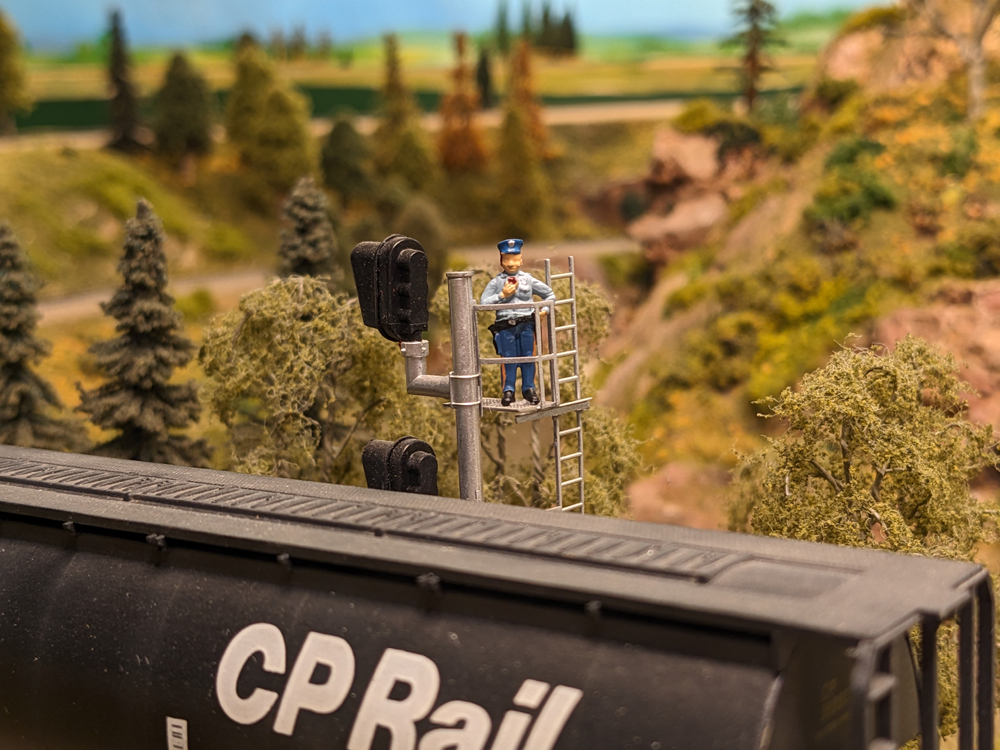 A model figure stands in an overwatch tower next to a model tank car on a model railroad layout