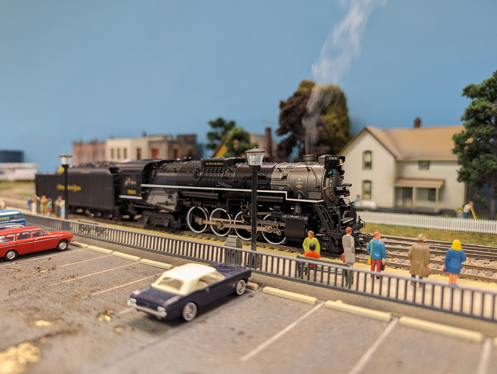 A black model steam locomotive in a town setting on a model railroad layout