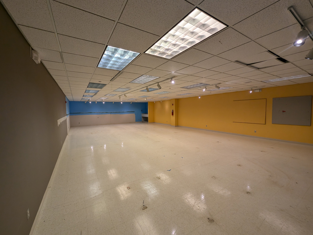 A now-empty room which formerly held a sprawling model railroad layout. The walls are yellow and blue. The floor and ceiling are white.