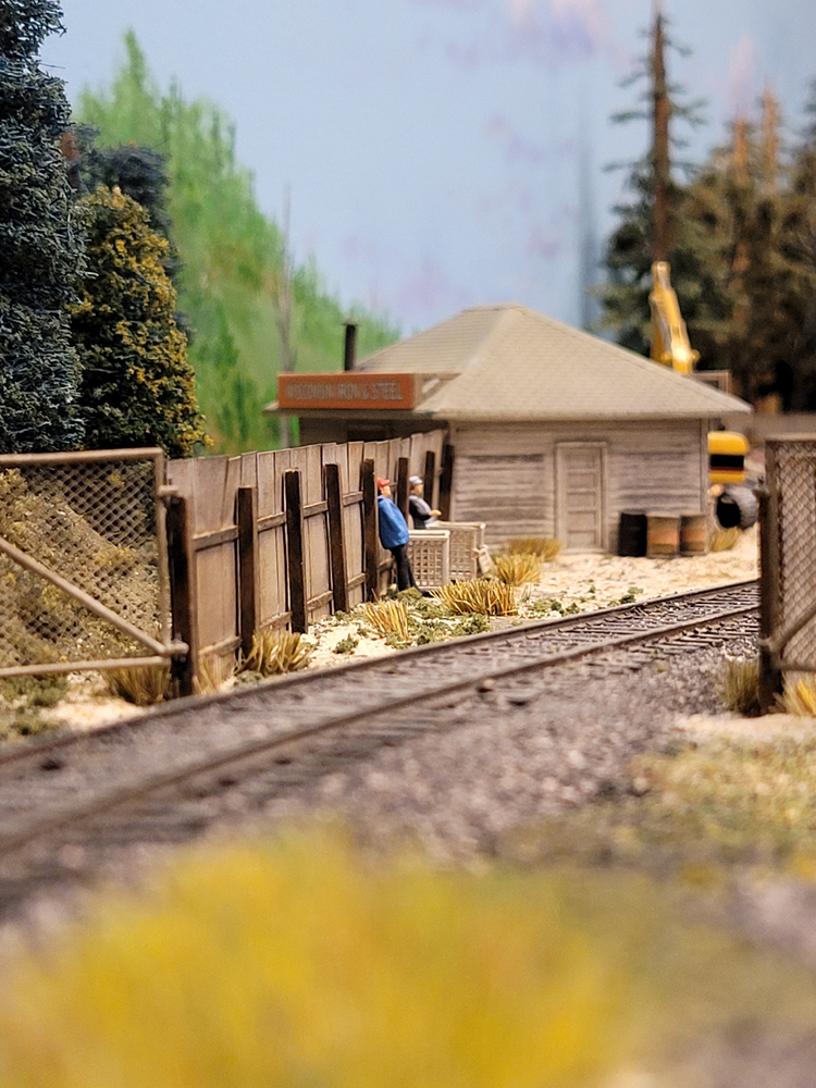 Two figures stand up in a model railroad scrap yard setting