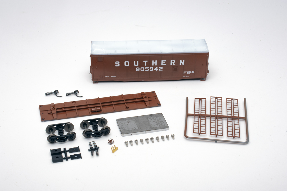 A disassembled model freight car in maroon with white lettering and roof