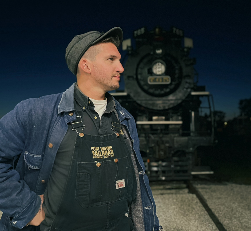 Man in period rail garb in front of steam locomotive