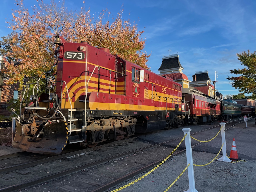 A maroon diesel with yellow stripes leads a line of passenger cars of different eras