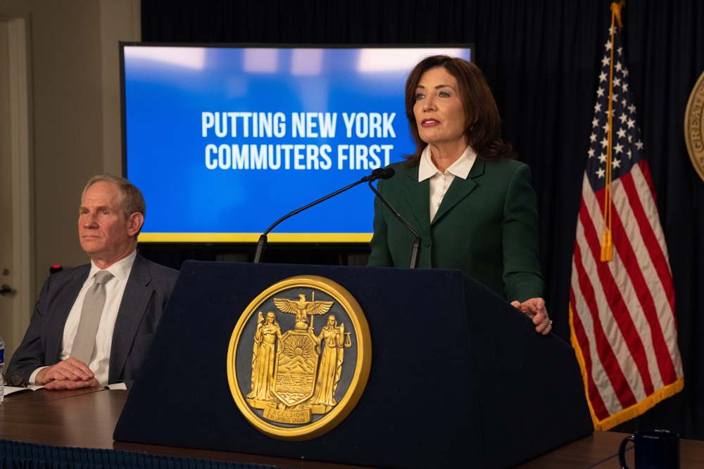 Woman at podium with screen in background reading "putting New York commuters first."