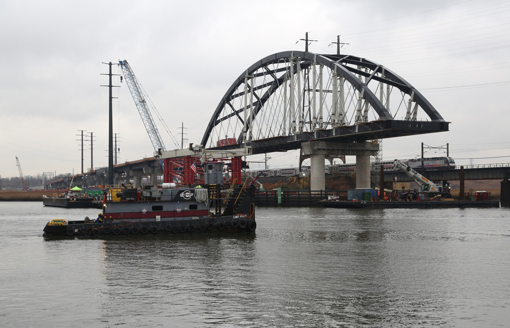 View of bridge under construction with tugboat in foreground