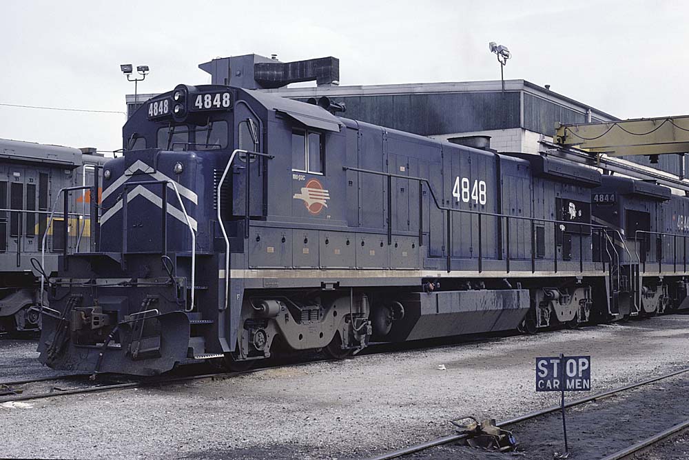 Dark blue diesel locomotive with red logo outside shop building