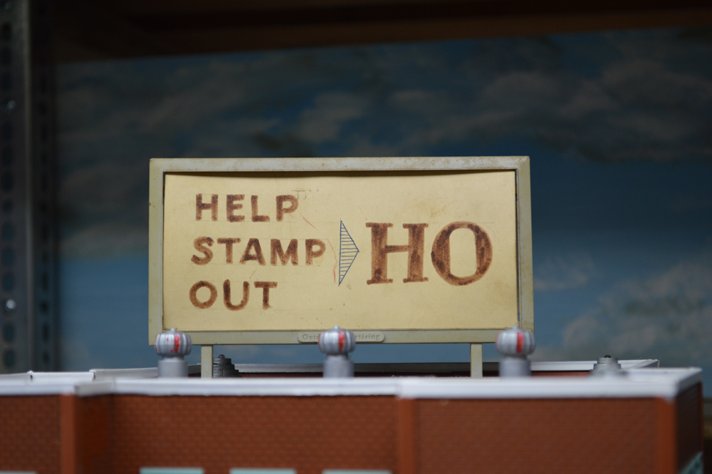 A sign on a model railroad layout which reads "Help stamp out HO"