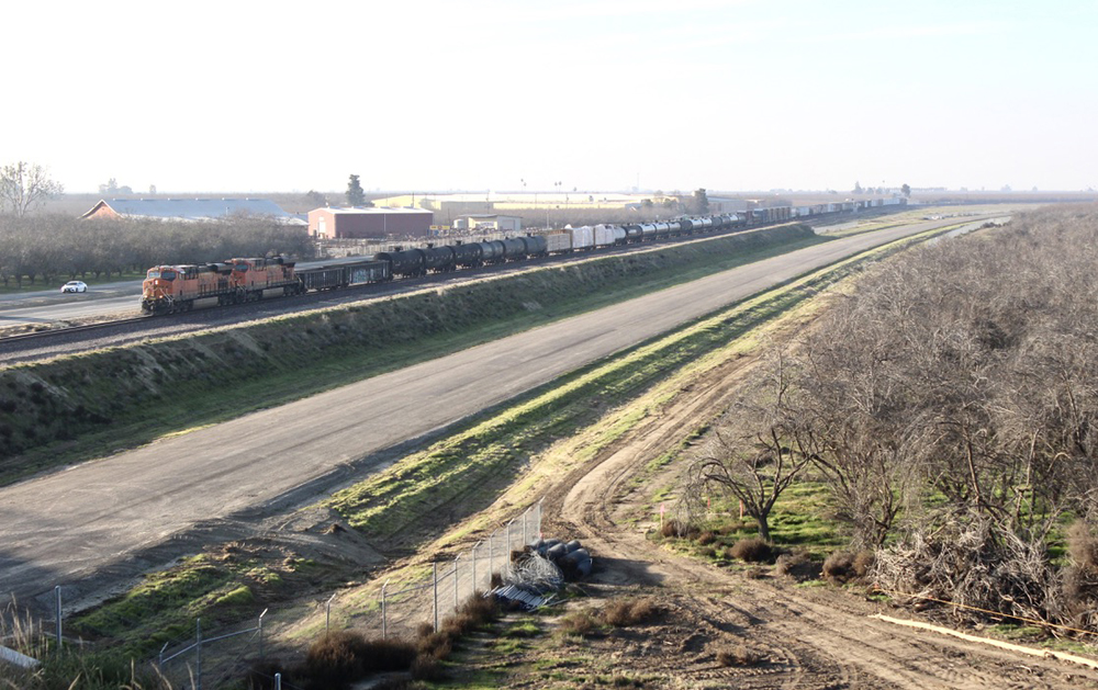 Freight train on long, flat, straight track next to area of future roadway