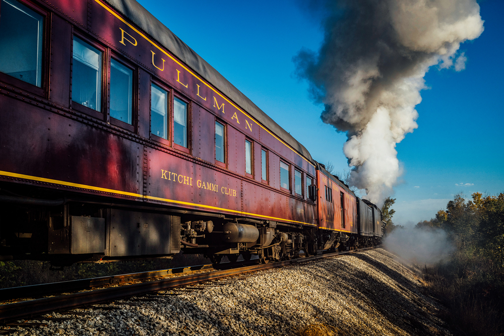 Maroon passenger car being pulled by steam locomotive