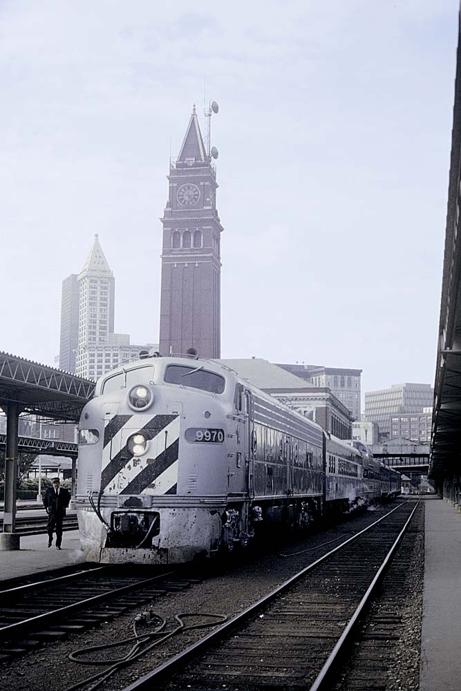 Silver-and-black diesel locomotive with passenger train at station with tower