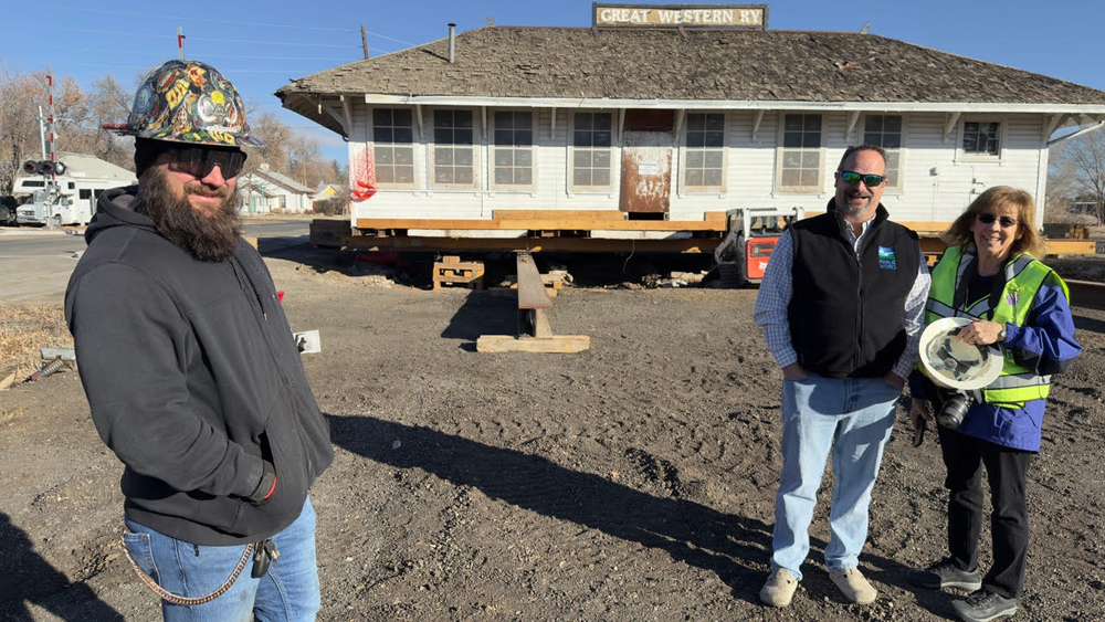 Three people in front of train station on wheels for relocation