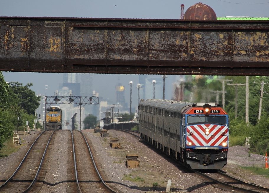 Commuter train passes under bridge with freight train in distance