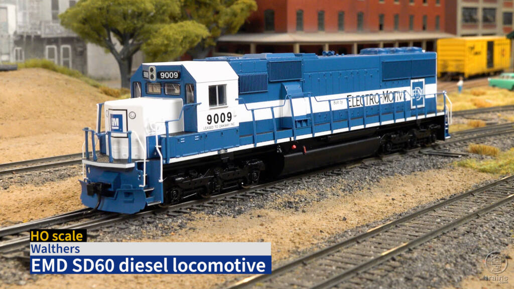 Screen capture from product review video showing HO scale diesel in blue and white paint on layout with title bar in lower left corner.