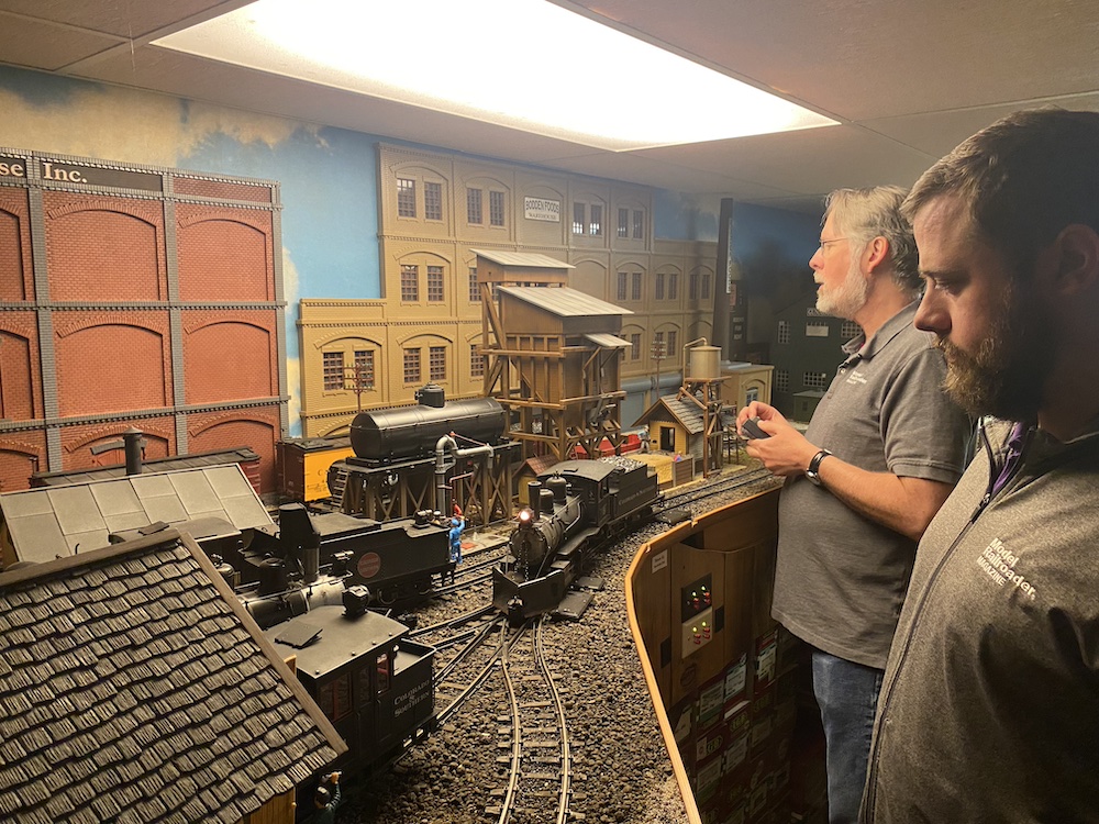 Two operators watch on as a steam locomotive arrives at an engine terminal