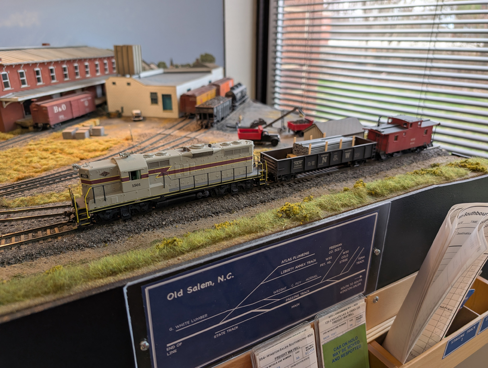 An HO scale GP7, gondola with pipe load, and caboose on a layout.