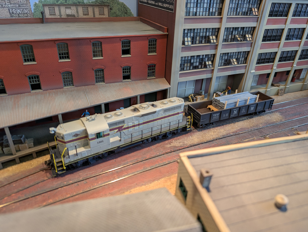 An HO scale GP7 and loaded gondola at a factory.