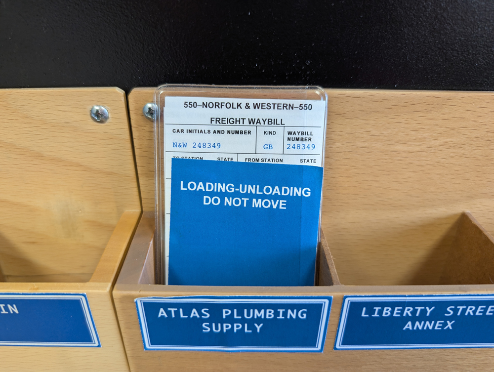 A model railroad car card with a blue tag in front of it in a card pocket