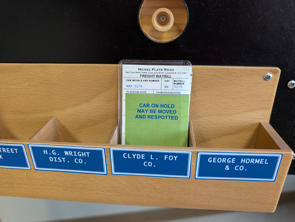 A model railroad car card with a green tag in front of it in a card pocket
