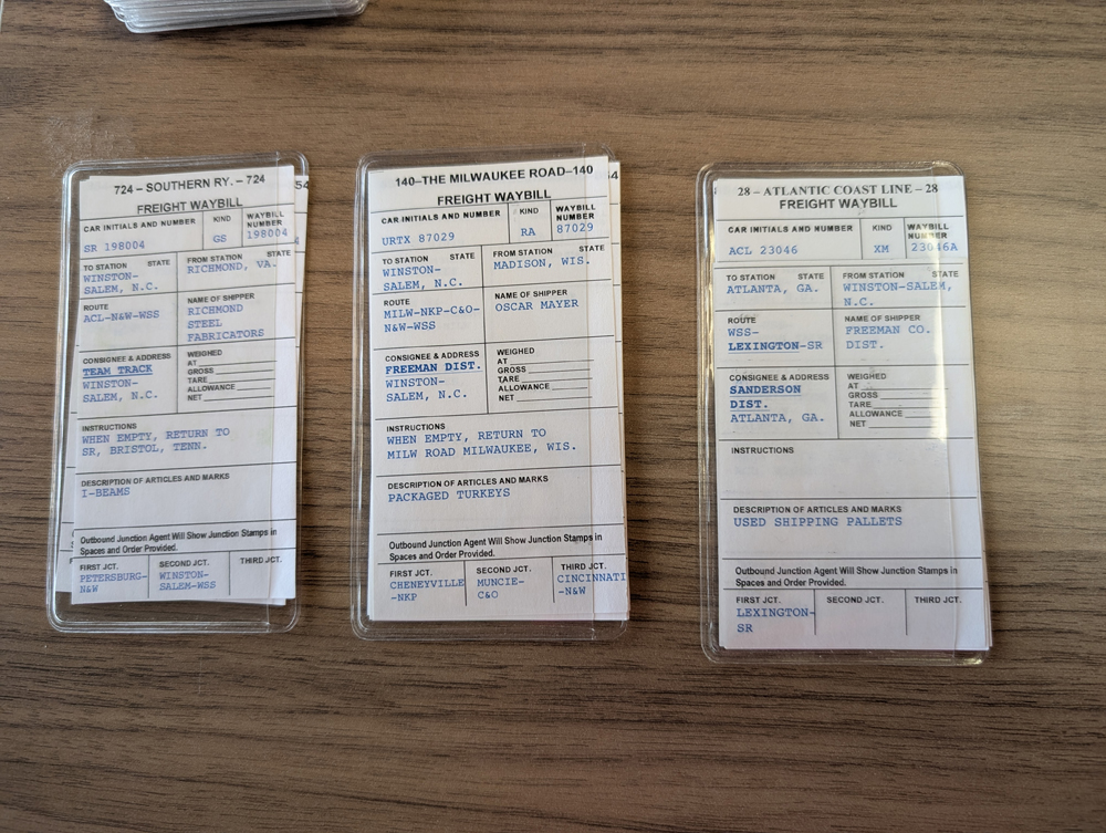 Three model railroad car cards with wood background