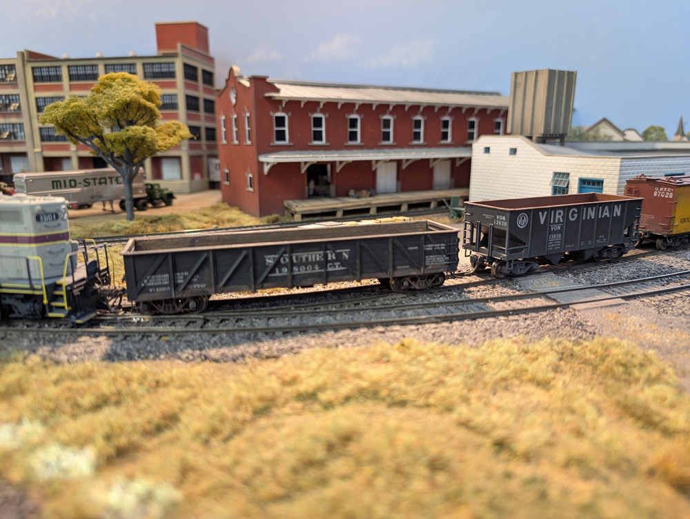 An HO scale GP7 with a gondola and hopper behind it