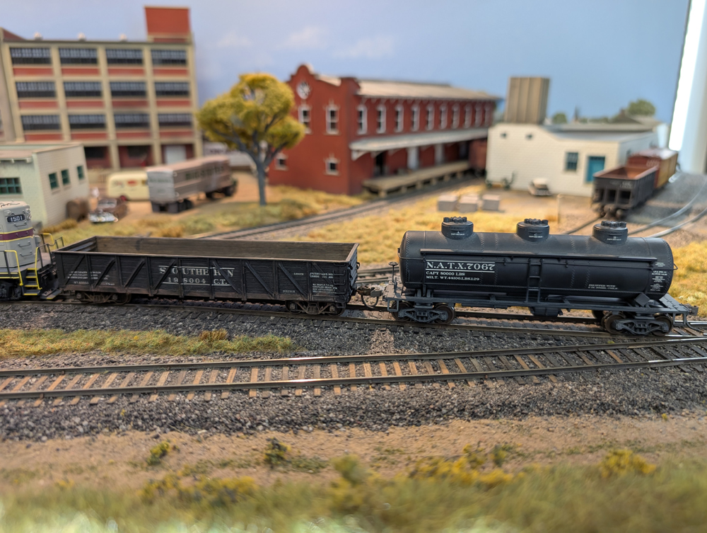 An HO scale GP7 with gondola and three-dome tank car behind