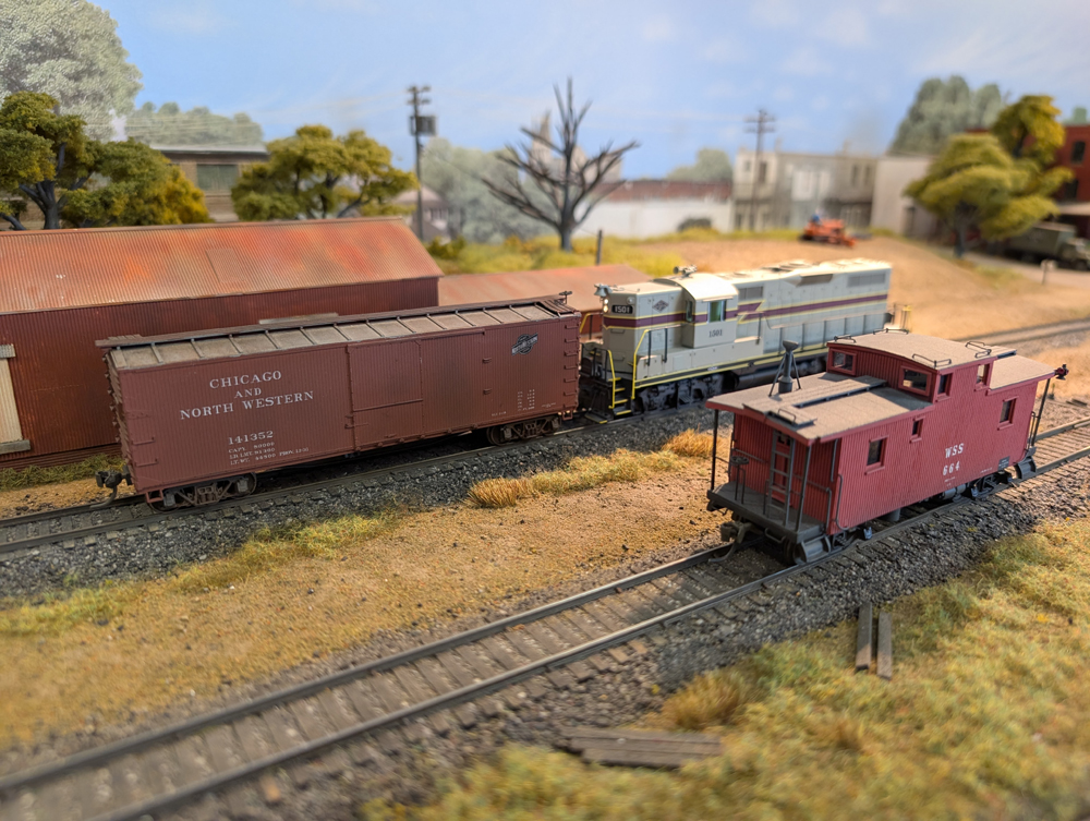 An HO scale GP7 picking up a boxcar from an industry with a caboose in front