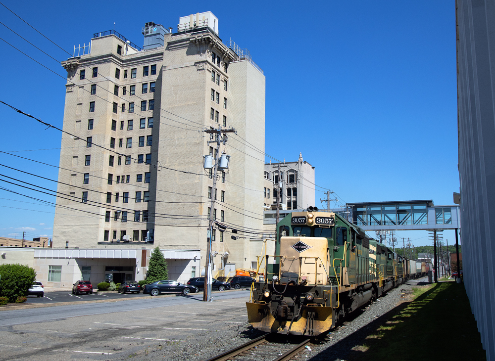 An 11 story office building next to tracks occupied by a train pulled by two green-and-yellow diesels.
