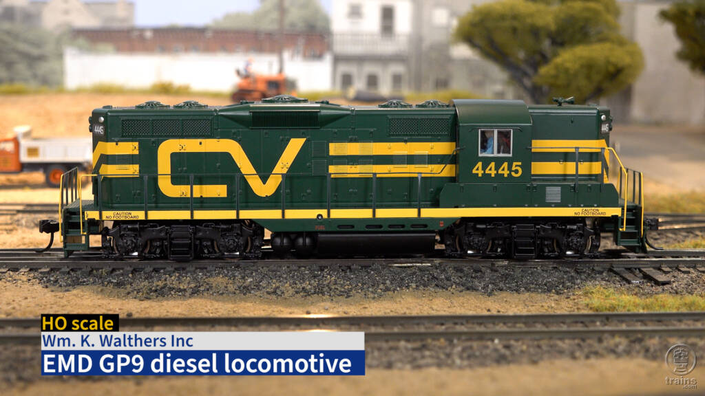 Side view of HO scale diesel locomotive painted green and yellow on scenicked model railroad with title bar in lower left corner.