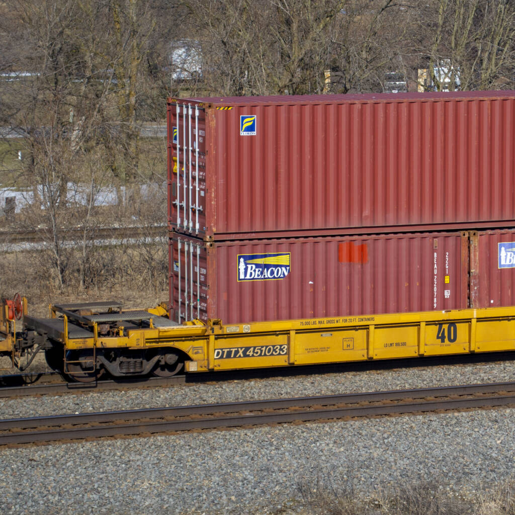 Color photo of yellow 40-foot well car with three mineral red intermodal containers.