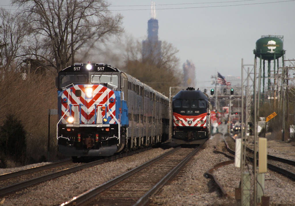 Commuter trains pass on three-track line with Willis Tower in distance