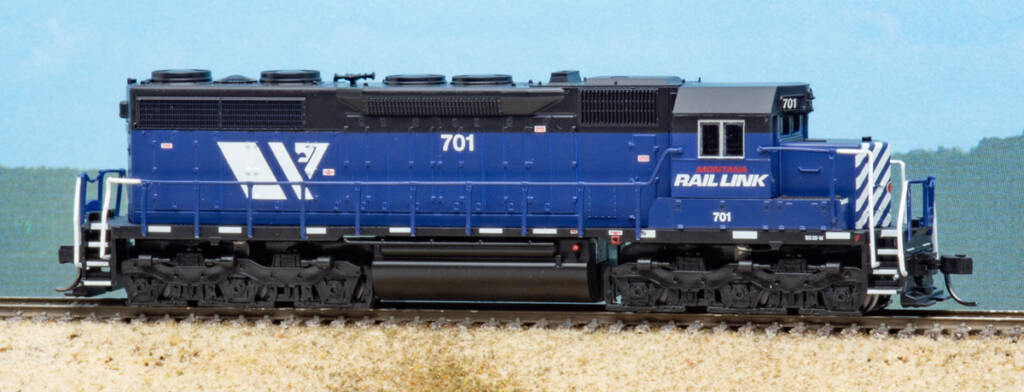 Color photo of N scale six-axle hood unit in blue and black paint on scenicked base with sky background.