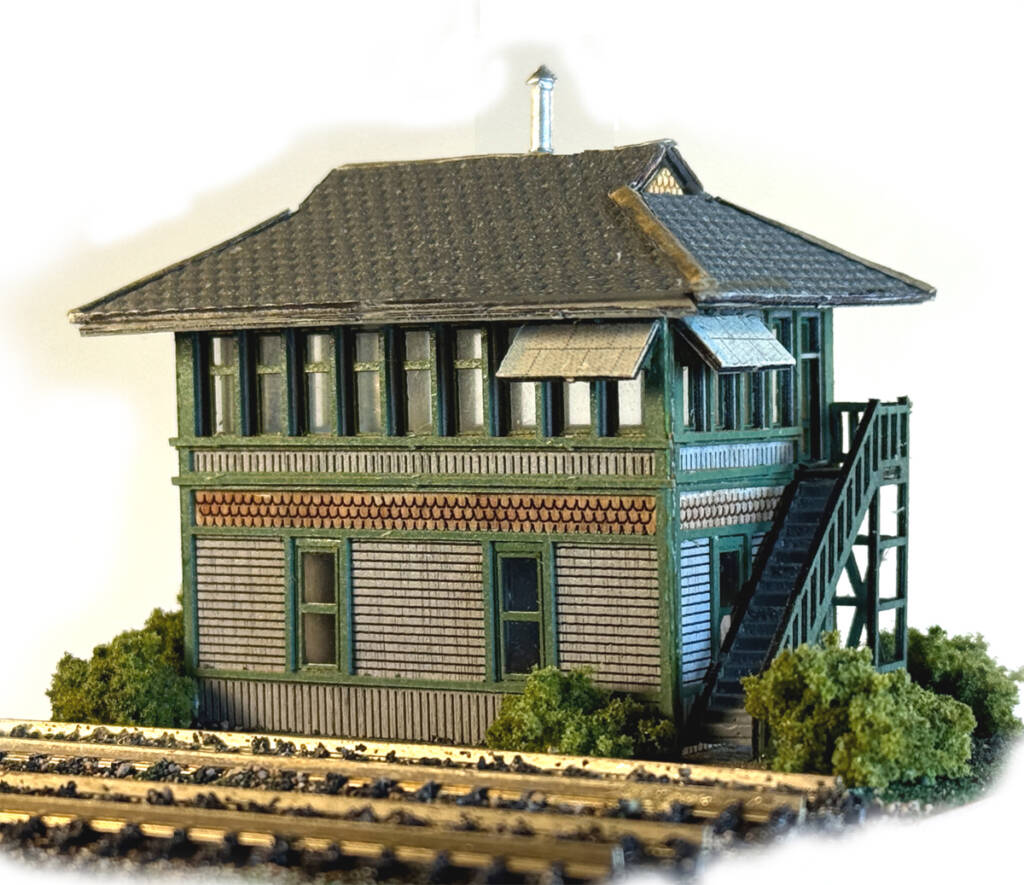 Color photo of N scale interlocking tower painted gray, green, and brown with track in foreground.