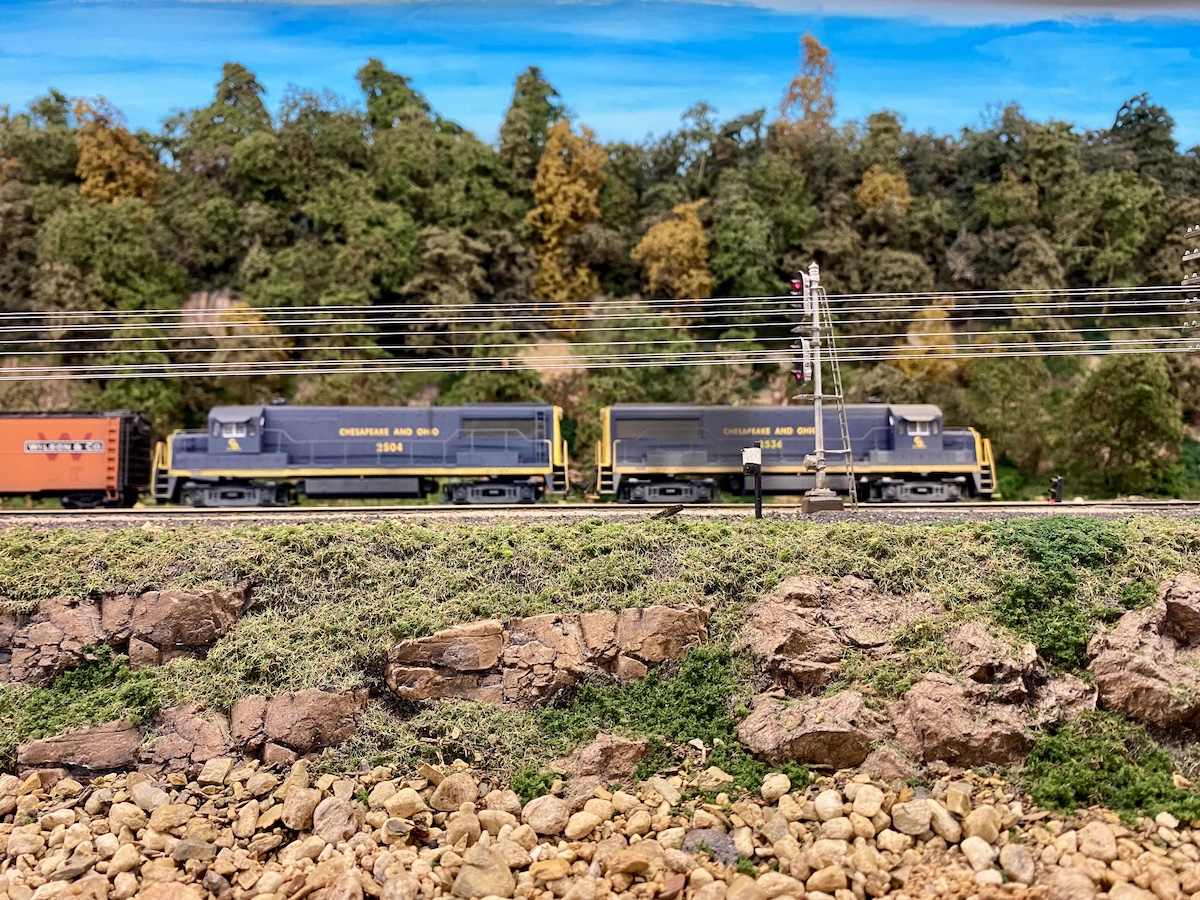 HO scale blue diesel-powered freight trains traverse past a river bank