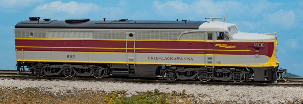 Color photo of HO scale six-axle cab unit painted gray, maroon, and yellow with black roof, trucks, and fuel tank on scenicked base with sky background