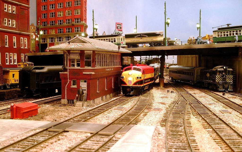 Two trains pass a switching tower on a model railroad layout