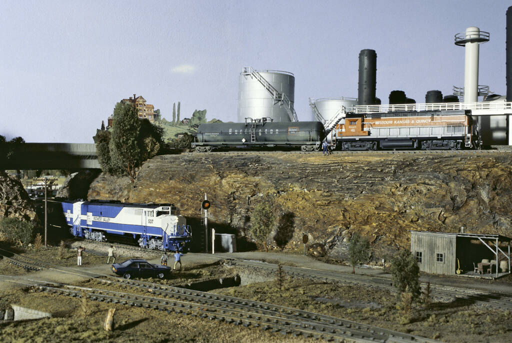 Multiple model locomotives and a chemical plant on a model railroad layout