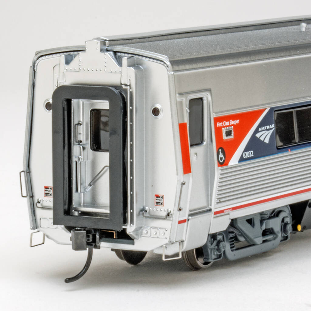 Color photo showing vestibule end of HO scale modern passenger car with metal finish; tinted windows; and red, white, and blue graphics.